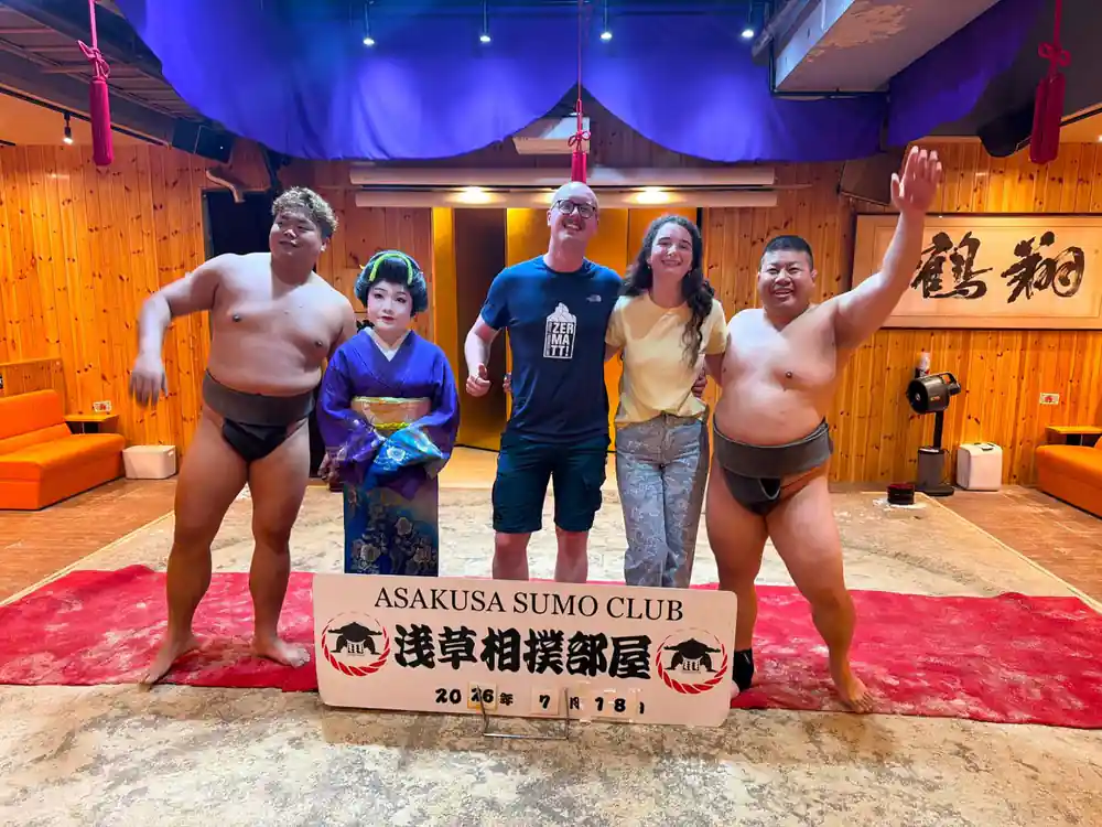 Group of five people posing with sumo club sign indoors