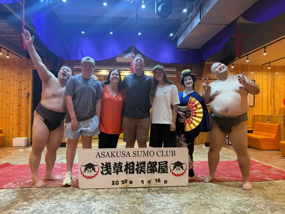 Group of people posing with sumo wrestlers and club sign