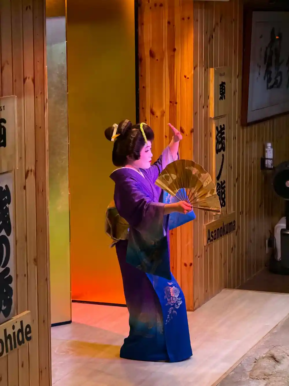 Person in blue kimono posing with decorative fan indoors