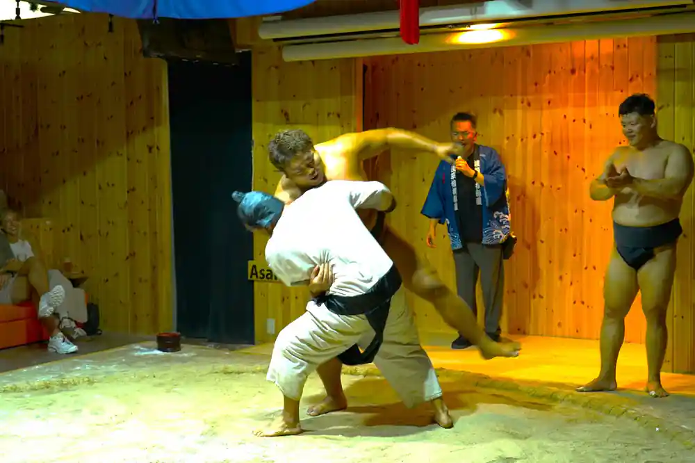 Sumo wrestler performing backflip indoors with spectators watching