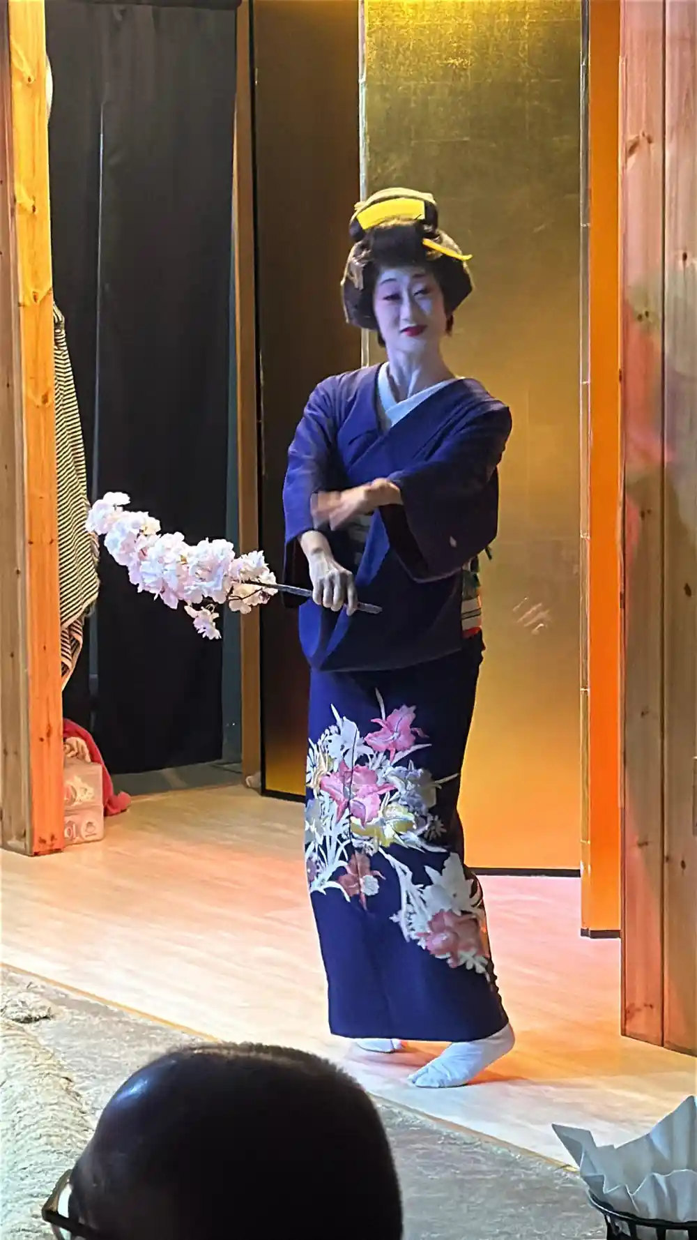 Woman in dark blue kimono with fan standing indoors